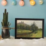 Vintage countryside wall art with hills, stream, and trees in soft green and blue tones by Infidu. displayed on the wall