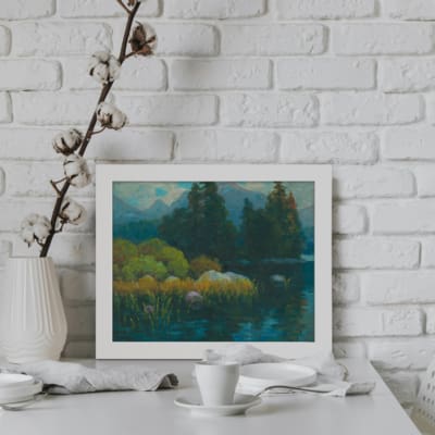 Vintage wall art featuring a serene nature scene with trees, a calm lake, and distant mountains. Perfect for home decor. displayed on the wall in a white frame