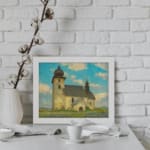 Vintage wall art of a rustic church in a calm countryside with a blue sky, white clouds, green grass, and touches of purple wildflowers. displayed on the wall