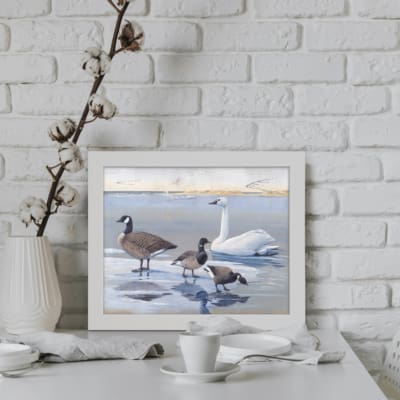 Vintage wall art featuring ducks, geese, and a serene lake with subtle reflections and a snowy background, creating a peaceful atmosphere. displayed on the wall in a white frame
