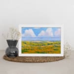 Infidu vintage wall art featuring a serene pastoral landscape with rolling hills, open fields, and soft clouds in the sky. displayed on the wall art in a white frame