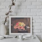 Vintage wall art of pink and yellow flowers in a white bowl with a brown textured background, framed in white. displayed on the wall