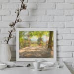 Vintage wall art of a sunny terrace with trees, wooden floor, and distant hills, capturing a peaceful outdoor scene. displayed on the wall