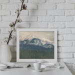Infidu vintage wall art of snowy mountains in soft blue tones with a misty sky and forested valley. displayed on the wall