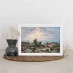 Vintage wall art of a rocky coast with calm blue water and a soft pastel sky in pink, cream, and blue tones. displayed on the wall