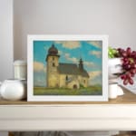 Vintage wall art of a rustic church in a calm countryside with a blue sky, white clouds, green grass, and touches of purple wildflowers. displayed on the wall