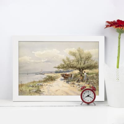Vintage wall art of a tranquil coastal landscape featuring a sandy path, water, a tree, and a serene blue sky. Perfect for calm home decor. displayed on the wall in a white frame