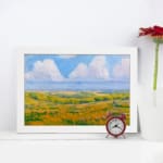Infidu vintage wall art featuring a serene pastoral landscape with rolling hills, open fields, and soft clouds in the sky. displayed on the wall art in a white frame