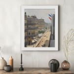 Vintage wall art of a Paris street scene with French flags, horse-drawn carriages, pedestrians, and elegant buildings in soft muted colors. displayed on the wall