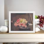 Vintage wall art of pink and yellow flowers in a white bowl with a brown textured background, framed in white. displayed on the wall