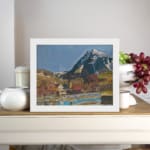 Vintage village at the base of snowy peaks with colorful houses, hills, and a serene river or pond. displayed on the wall