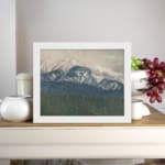Infidu vintage wall art of snowy mountains in soft blue tones with a misty sky and forested valley. displayed on the wall