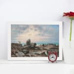 Vintage wall art of a rocky coast with calm blue water and a soft pastel sky in pink, cream, and blue tones. displayed on the wall