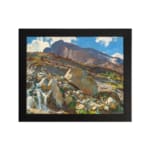 Vintage wall art of a mountain landscape with a waterfall, earthy rocks, green hills, and a blue sky with white clouds. hung on the wall