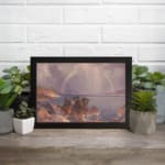 Vintage wall art of a calm lake with a rainbow, mountains, and soft sunlight. displayed on the wall