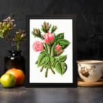 Vintage wall art of soft pink rosebuds with green leaves and stems in a black frame on a white background. displayed on the wall