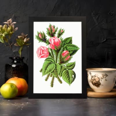 Vintage wall art of soft pink rosebuds with green leaves and stems in a black frame on a white background. displayed on the wall