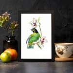 A green bird perched on a branch with white flowers, set on a white background and framed in black. displayed on the wall