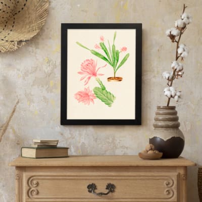 Vintage wall art with pink flowers and green cactus stems in a brown pot, set against a beige background with a clean black frame. displayed on the wall