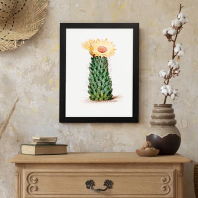 Vintage wall art of a cactus with a yellow flower in bloom, set against a light cream background, framed in black. displayed on the wall