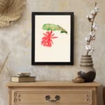 Vintage wall art with a red hanging flower and green leaf on a cream background, framed in black. displayed on the wall