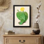 Vintage cactus wall art with a green cactus and yellow flower on a beige background, framed in black. displayed on the wall