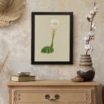Vintage wall art with a round green cactus and a tall white flower with pink and yellow accents, on a beige background, framed in black. displayed on the wall