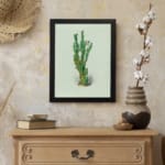 Vintage wall art of a green plant with small leaves, set against a soft light cream background, framed in black. displayed on the wall