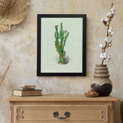Vintage wall art of a green plant with small leaves, set against a soft light cream background, framed in black. displayed on the wall