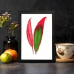 Vintage wall art of bold red and green tropical leaves in a black frame displayed on the wall