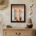 Vintage architectural wall art with two traditional figures, colorful tile patterns, and detailed building elements in black frame. displayed on the wall