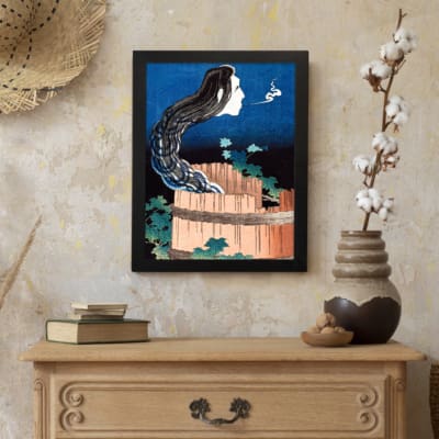 Vintage wall art of a ghostly face with long black hair emerging from a wooden barrel, with a dramatic night sky background. displayed on the wall in a black frame