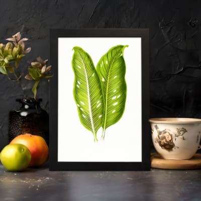 Vintage wall art featuring two large tropical green leaves with white lines and holes, set against a plain white background in a black frame. displayed on the wall
