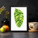 Bright green leaf with light and dark tones on white background in a black frame – vintage wall art by Infidu. displayed on the wall