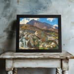 Vintage wall art of a mountain landscape with a waterfall, earthy rocks, green hills, and a blue sky with white clouds. displayed on the wall