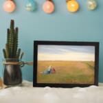 Vintage wall art of two women sitting in an open field under a bright, cloudy sky with soft green and yellow tones. displayed on the wall