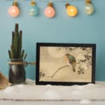 Infidu vintage wall art featuring a delicate bird perched on a branch with small leaves against a soft, neutral background. displayed on the wall art in a black frame