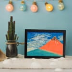 Vintage wall art of Mount Fuji by Hokusai with red mountain, blue sky, and white clouds. displayed on the wall