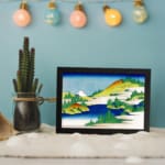 Infidu vintage wall art featuring a serene mountain lake with towering peaks, calm reflective waters, and surrounding trees. displayed on the wall art in a black frame