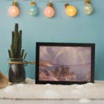 Vintage wall art of a calm lake with a rainbow, mountains, and soft sunlight. displayed on the wall