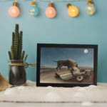 Infidu vintage wall art featuring a mysterious scene of a lion standing beside a sleeping person under a full moon in a serene, dreamlike landscape. displayed on the wall art in a black frame