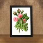 Vintage wall art of soft pink rosebuds with green leaves and stems in a black frame on a white background. displayed on the wall