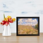 Vintage wall art of a golden grass field under a blue sky with white clouds and trees on the side displayed on the wall