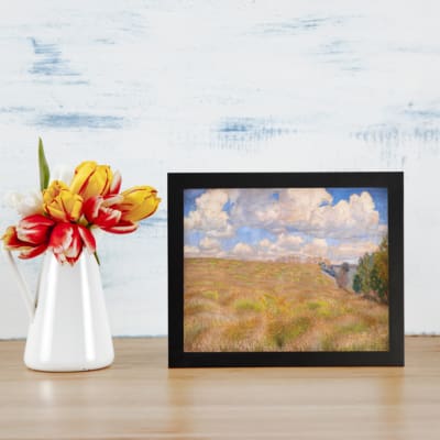 Vintage wall art of a golden grass field under a blue sky with white clouds and trees on the side displayed on the wall