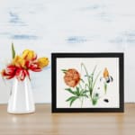 Vintage botanical wall art with orange peony, yellow and purple iris, and green leaves, featuring small insects, framed in black. displayed on the table