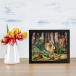 Vintage wall art of a brown rabbit sitting in a lush green forest with trees and plants in the background. displayed on the wall