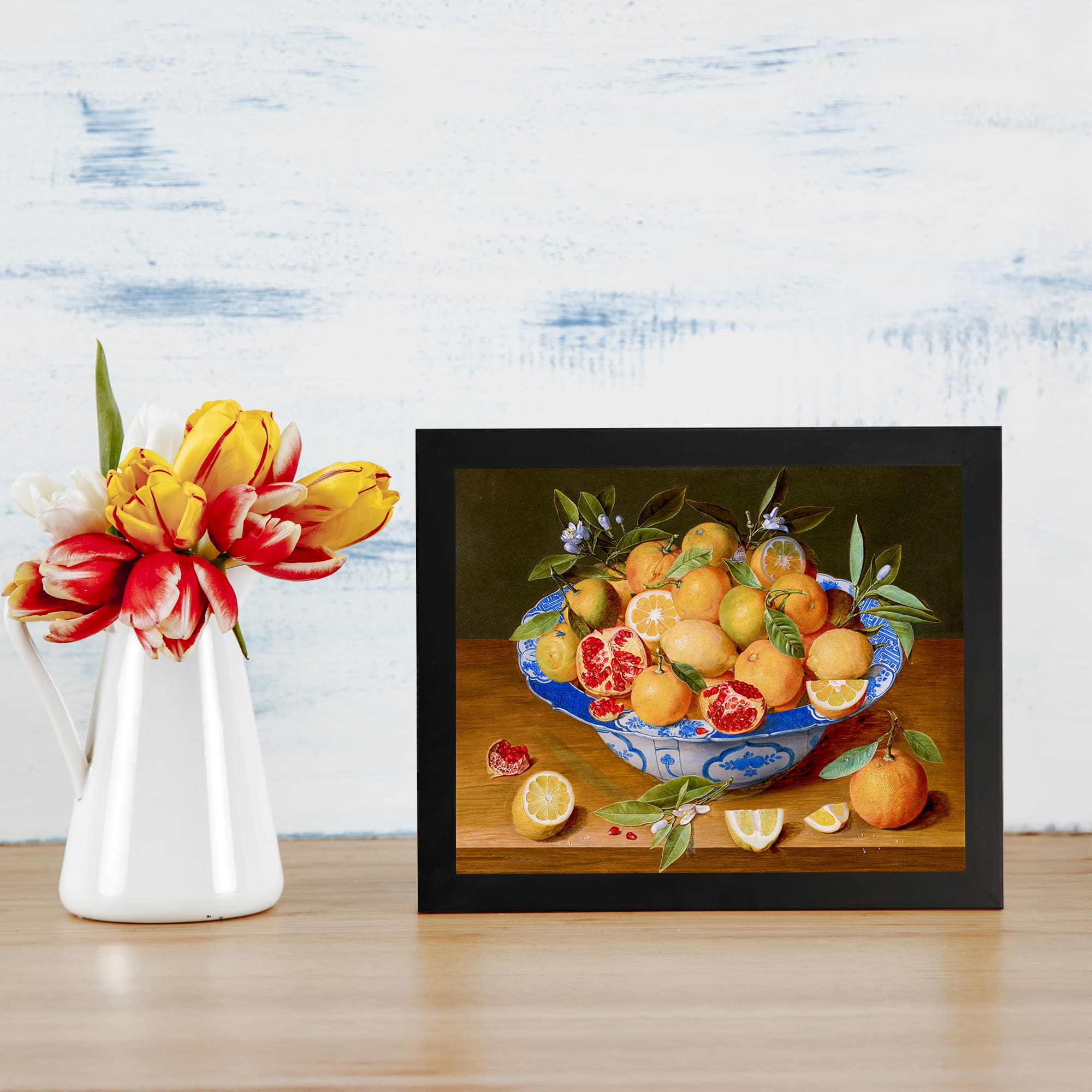 Vintage wall art of blue bowl filled with oranges, lemons, and pomegranate on wooden table with dark olive green background. displayed on the wall