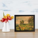 Infidu Countryside vintage wall art showing a sunset glow over winding paths, green hills, trees, people, cows, and horses by a calm river. displayed on the wall
