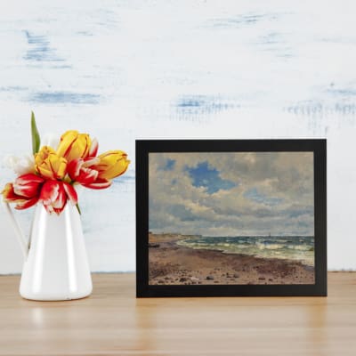 Infidu vintage wall art featuring a serene seascape with ocean waves, blue sky, and sandy shoreline. Ideal for vintage wall decor. displayed on the table in a black frame