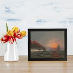 Vintage wall art showing a dramatic ocean sunset with tall waves, sailing ships, glowing cliffs, and a cloudy sky. displayed on the wall
